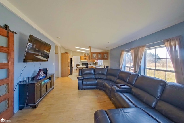 living area featuring vaulted ceiling, a barn door, and light wood-type flooring