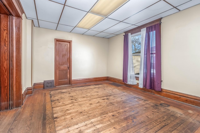 empty room featuring a drop ceiling, visible vents, baseboards, and hardwood / wood-style floors