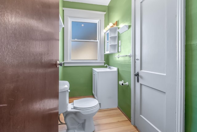 half bathroom featuring toilet, wood finished floors, and a sink