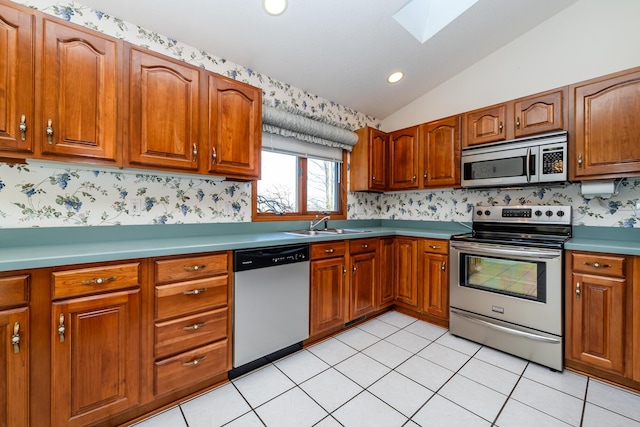 kitchen with a sink, lofted ceiling with skylight, appliances with stainless steel finishes, and brown cabinetry