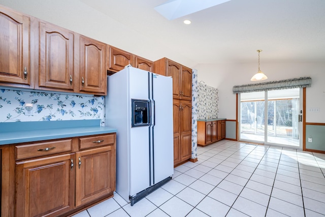 kitchen with decorative light fixtures, light tile patterned flooring, brown cabinetry, and white fridge with ice dispenser