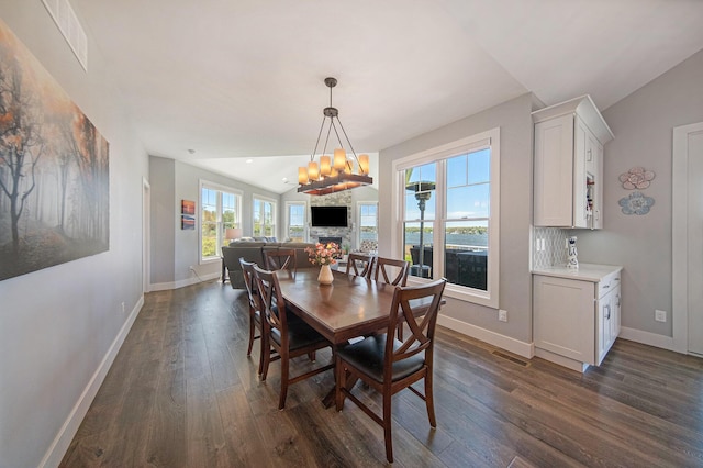 dining space featuring a stone fireplace, a notable chandelier, dark wood finished floors, and baseboards