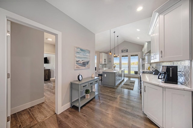 kitchen with a kitchen island with sink, white cabinetry, light countertops, lofted ceiling, and dark wood-style flooring