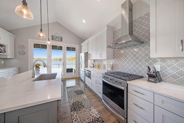 kitchen featuring lofted ceiling, an island with sink, a sink, stainless steel appliances, and wall chimney exhaust hood