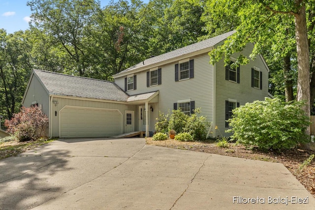 colonial-style house featuring an attached garage, concrete driveway, and a shingled roof