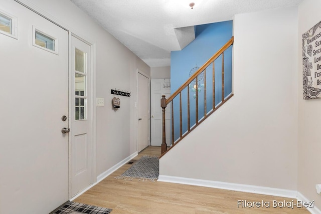 foyer with baseboards, wood finished floors, and stairs