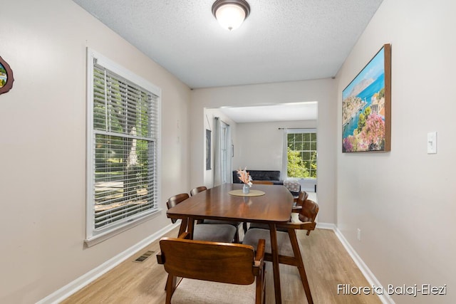 dining area featuring baseboards, light wood finished floors, and a textured ceiling