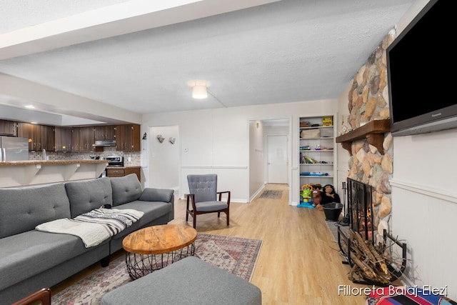 living room featuring a stone fireplace, light wood-type flooring, and a textured ceiling