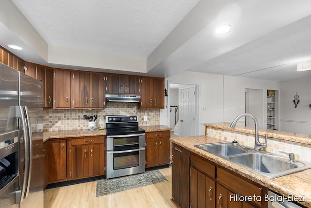 kitchen featuring under cabinet range hood, light countertops, light wood-style flooring, appliances with stainless steel finishes, and a sink