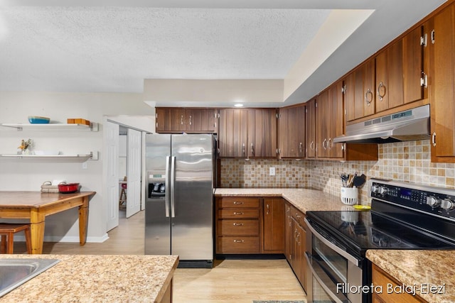 kitchen with light wood finished floors, light countertops, under cabinet range hood, appliances with stainless steel finishes, and tasteful backsplash