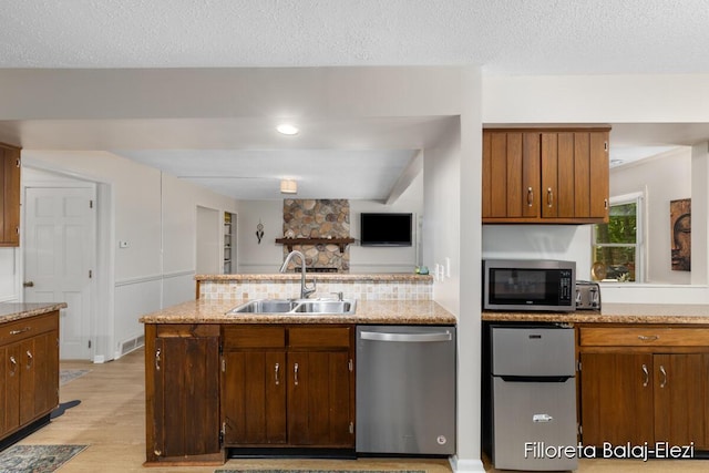 kitchen featuring a sink, a textured ceiling, stainless steel appliances, light wood-style floors, and a peninsula