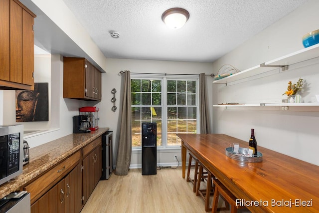 kitchen featuring light wood finished floors, stainless steel microwave, baseboards, a textured ceiling, and open shelves