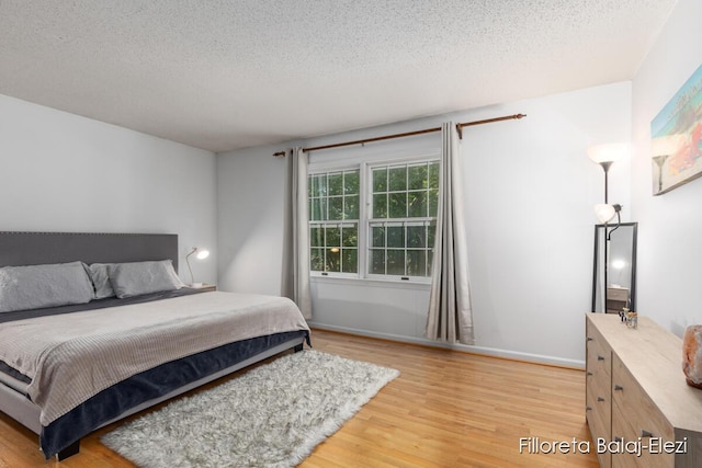 bedroom with baseboards, a textured ceiling, and light wood-style floors