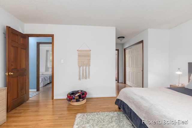 bedroom with a closet, light wood-type flooring, and baseboards