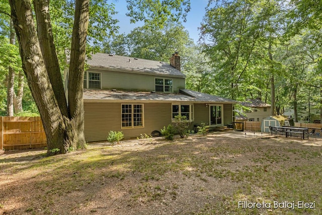 rear view of property with fence, a shed, a chimney, an outdoor structure, and a patio