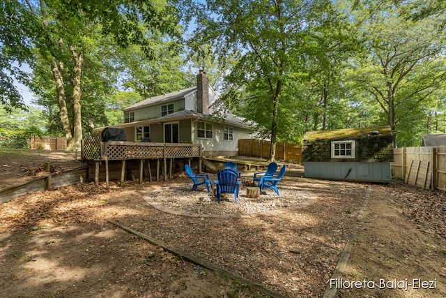 back of property with an outbuilding, a wooden deck, a fenced backyard, a chimney, and a fire pit