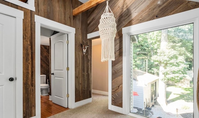 interior space featuring vaulted ceiling, carpet, wood walls, and a chandelier