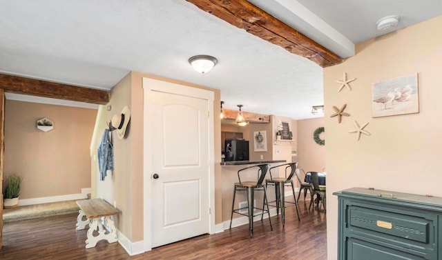 interior space featuring baseboards, dark wood finished floors, a breakfast bar, beam ceiling, and freestanding refrigerator