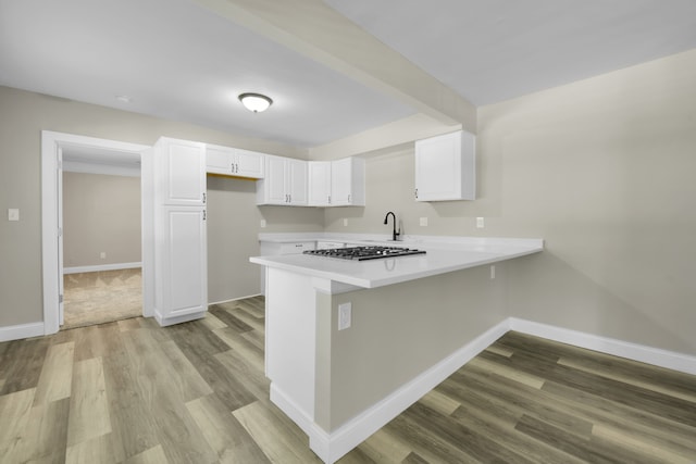 kitchen with wood finished floors, baseboards, stainless steel gas cooktop, a peninsula, and white cabinets