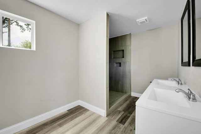 full bathroom featuring a tile shower, wood finished floors, baseboards, and a sink