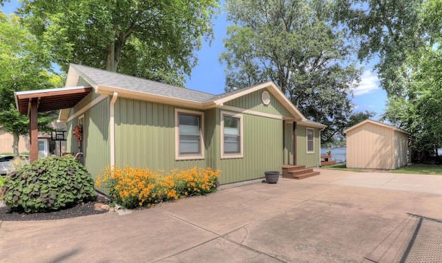 view of side of property featuring roof with shingles, entry steps, an outdoor structure, a storage shed, and a patio area