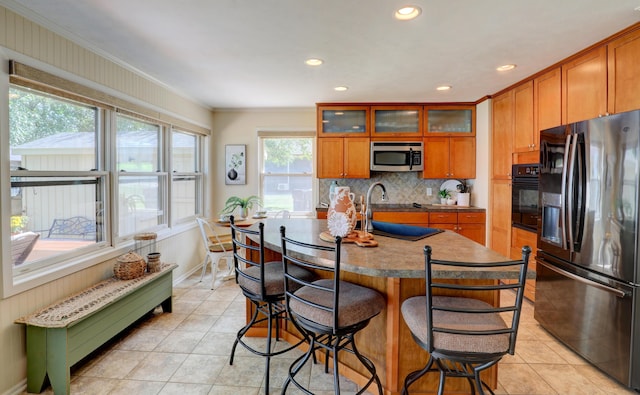 kitchen featuring brown cabinets, ornamental molding, a kitchen breakfast bar, tasteful backsplash, and stainless steel appliances