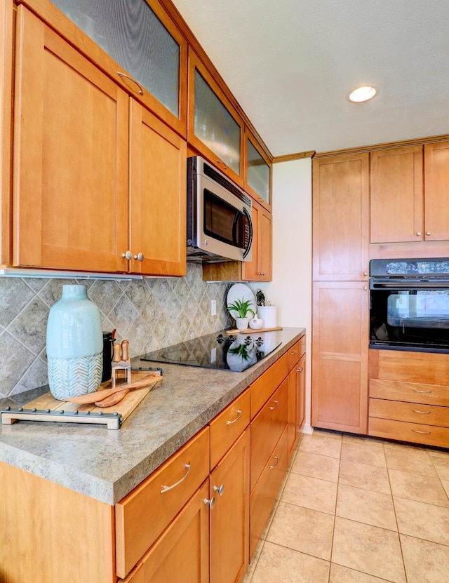 kitchen with brown cabinets, black appliances, backsplash, light tile patterned floors, and glass insert cabinets