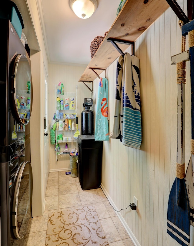 laundry room featuring laundry area, tile patterned flooring, stacked washer / drying machine, wood walls, and crown molding