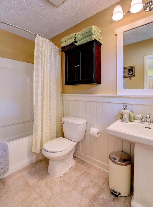 bathroom with tile patterned floors, toilet, a textured ceiling, wainscoting, and shower / bath combination with curtain