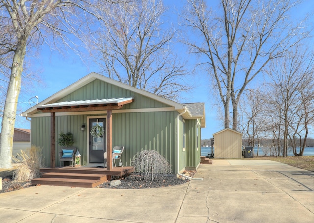 view of front facade featuring an outbuilding, driveway, a porch, a storage unit, and board and batten siding