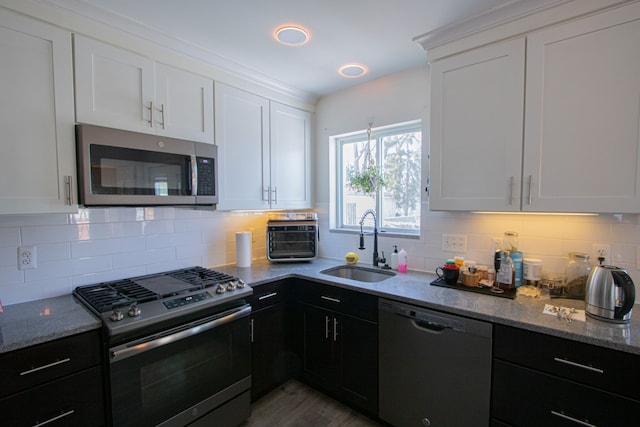 kitchen with a sink, dark cabinetry, stainless steel appliances, white cabinets, and light stone countertops