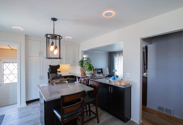 kitchen featuring visible vents, a breakfast bar, light stone counters, white cabinetry, and light wood-style floors