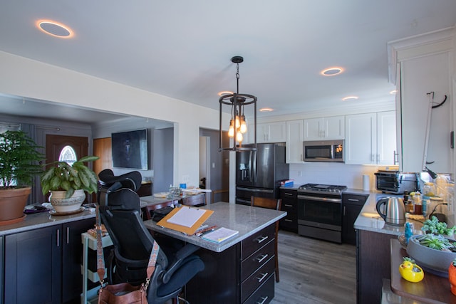 kitchen with a kitchen bar, decorative backsplash, wood finished floors, white cabinets, and stainless steel appliances