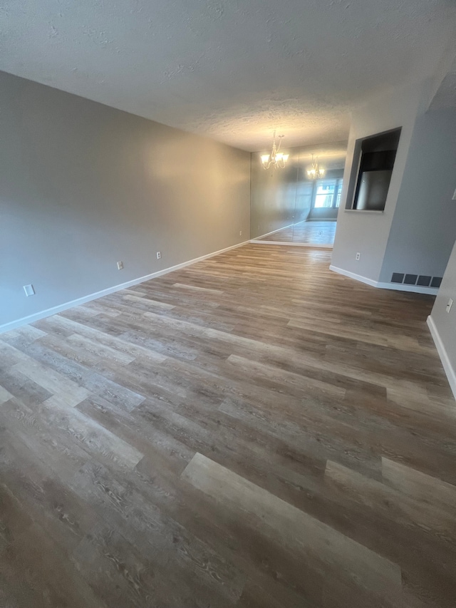 unfurnished room with visible vents, a notable chandelier, a textured ceiling, wood finished floors, and baseboards