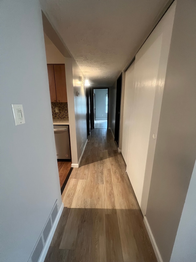 hall with baseboards, visible vents, and light wood finished floors