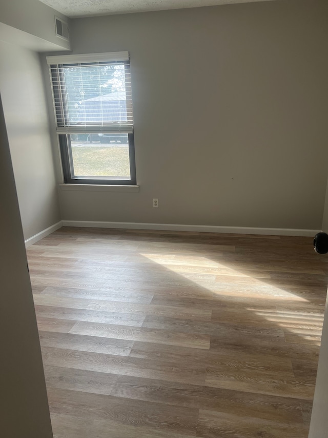 empty room featuring wood finished floors, visible vents, and baseboards