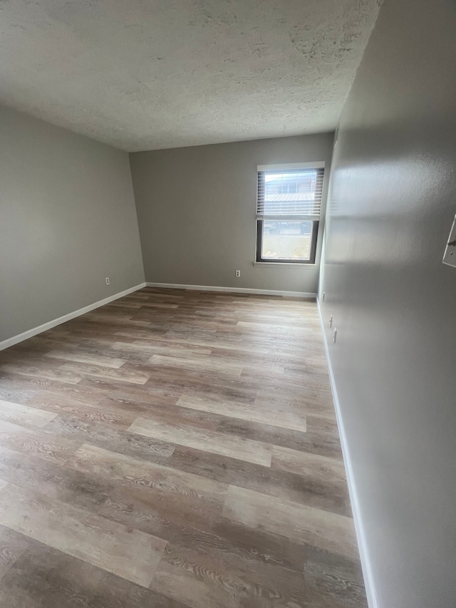 unfurnished room with light wood-style floors, baseboards, and a textured ceiling