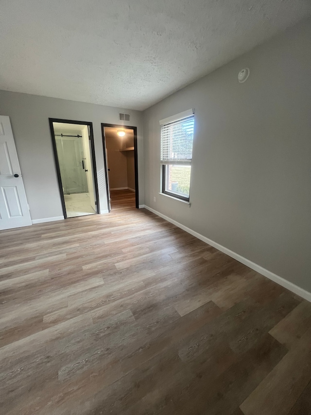 unfurnished bedroom featuring visible vents, baseboards, a textured ceiling, and light wood-style flooring