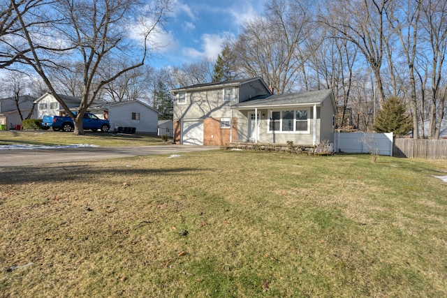 split level home with a front yard, fence, driveway, an attached garage, and brick siding