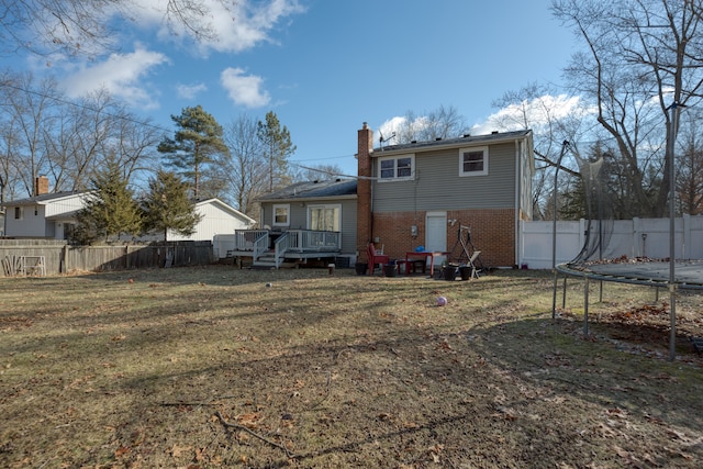 rear view of house featuring a trampoline, a fenced backyard, a yard, brick siding, and a chimney