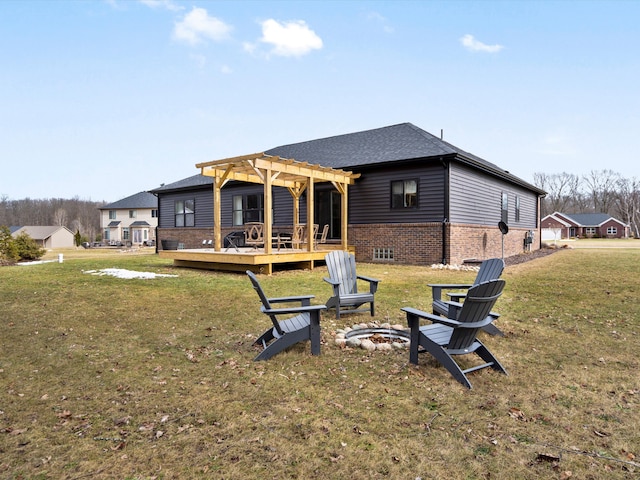 back of property with a lawn, a pergola, a fire pit, a wooden deck, and brick siding