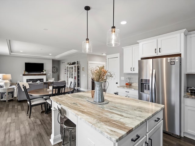 kitchen with a kitchen island, a fireplace, stainless steel fridge with ice dispenser, dark wood-style flooring, and a raised ceiling