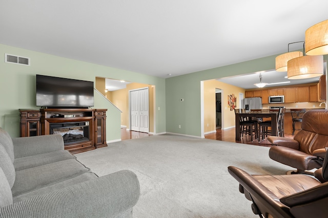 living area with a glass covered fireplace, baseboards, visible vents, and carpet floors