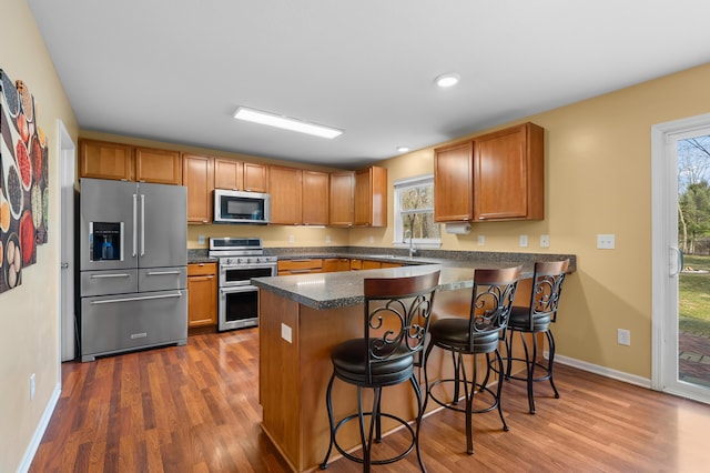 kitchen with a peninsula, dark countertops, dark wood-style flooring, and stainless steel appliances