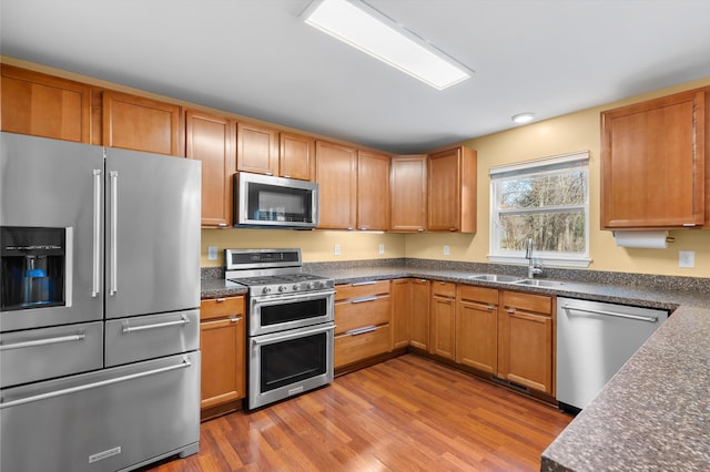 kitchen featuring dark countertops, wood finished floors, stainless steel appliances, and a sink