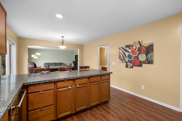 kitchen with baseboards, dark wood finished floors, brown cabinets, dark stone countertops, and hanging light fixtures