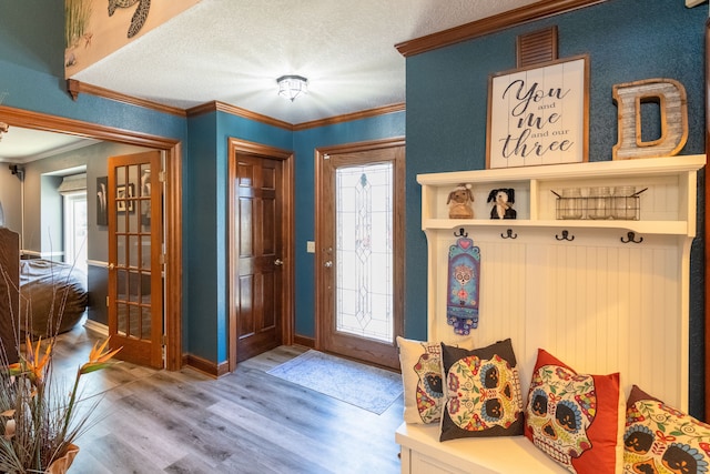 interior space with visible vents, a textured ceiling, wood finished floors, crown molding, and baseboards