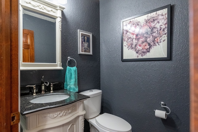 half bath with vanity, toilet, and a textured wall