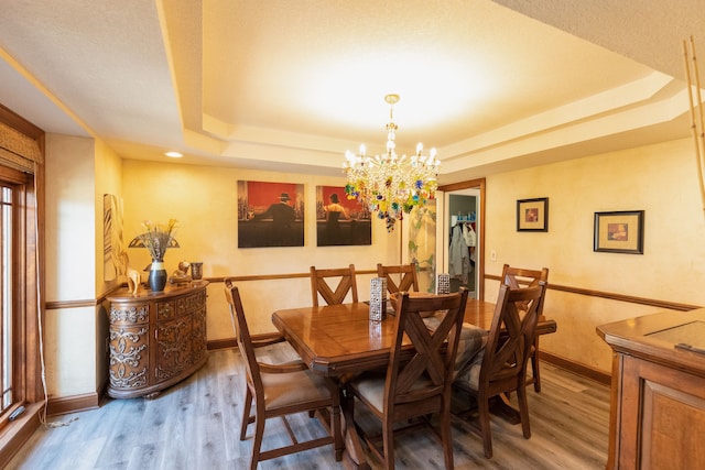 dining space with a tray ceiling, baseboards, an inviting chandelier, and wood finished floors