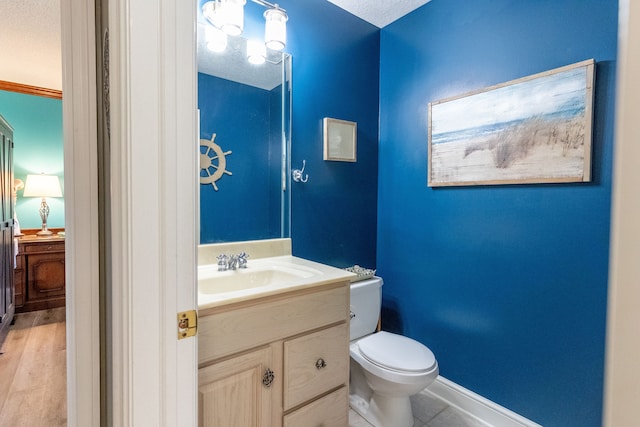 half bath featuring baseboards, toilet, vanity, and a textured ceiling